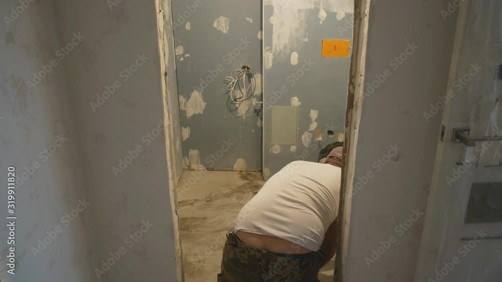 A guest worker kneeling makes marks on the concrete floor. Floor repair.back view A guest worker kneeling makes marks on the concrete floor. Floor repair.back view