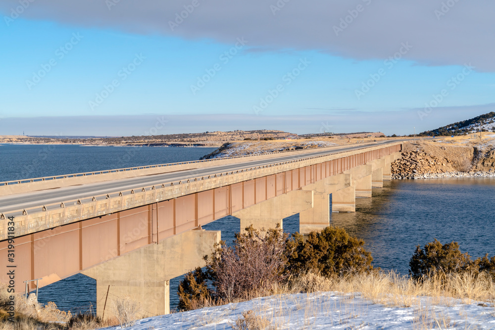 Massive bridge over a calm blue lake amid snow covered land in winter Massive bridge over a calm blue lake amid snow covered land in winter