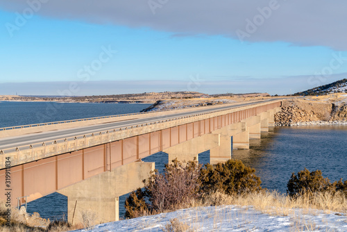 Massive bridge over a calm blue lake amid snow covered land in winter © Jason