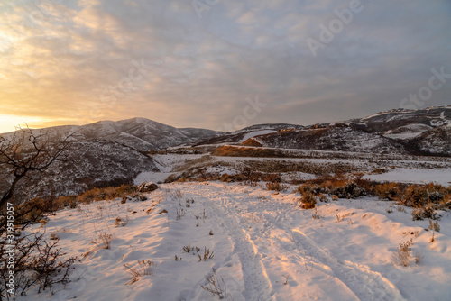 Hills with layer of fresh white snow against cloudy winter sky at sunset