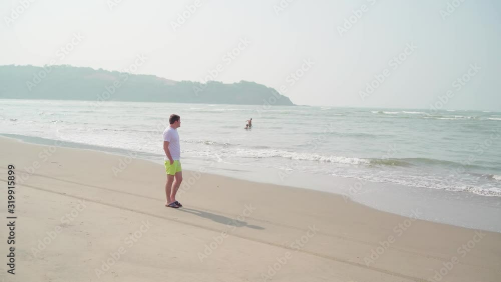 Traveling young man walking along sea coast. Male tourist promenading while resting on sandy beach near waving sea. Traveling young man walking along sea coast. Male tourist promenading while resting on sandy beach near waving sea.