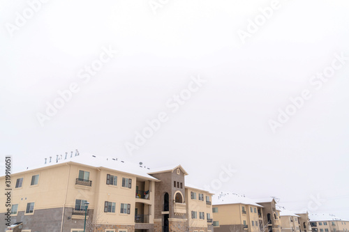 Facade of homes with snow coated roofs against cloudy sky on a cold winter day © Jason