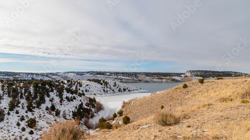 Panorama Scenic winter landscape with calm lake amid hills blanketed with white snow