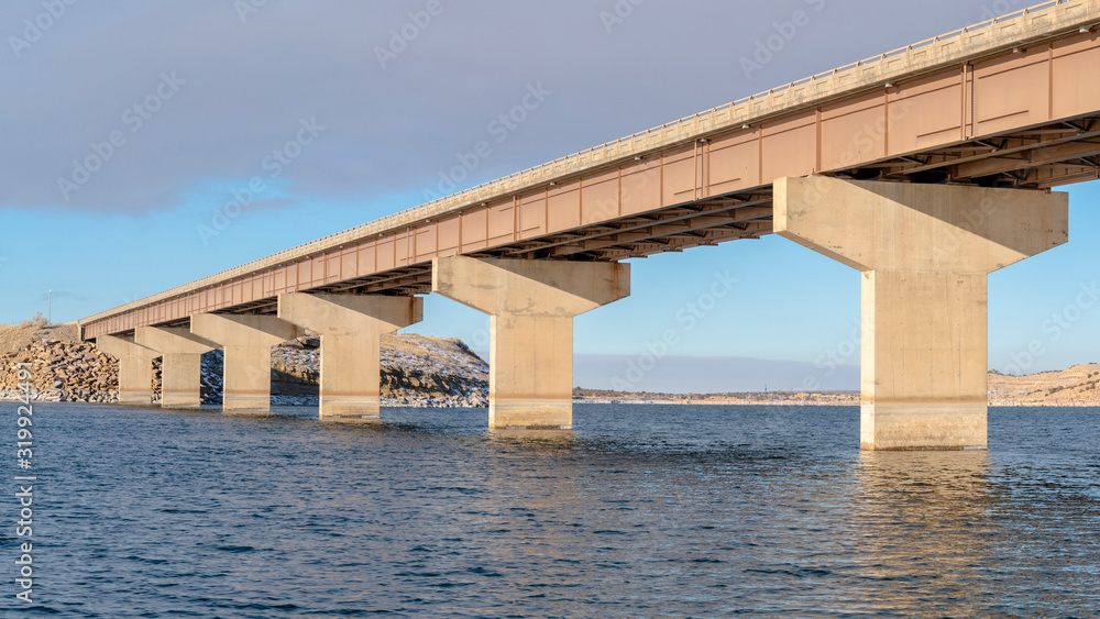 Panorama Stringer bridge spanning over a lake with view of snowy terrain and cloudy sky Panorama Stringer bridge spanning over a lake with view of snowy terrain and cloudy sky