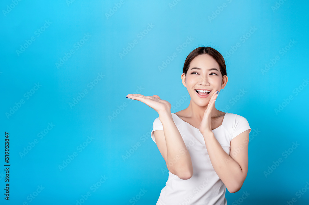 Beautiful young asian stand and pointing to copy space with big smile happy beaming face in seamless blue isolated background. Beautiful young asian stand and pointing to copy space with big smile happy beaming face in seamless blue isolated background.