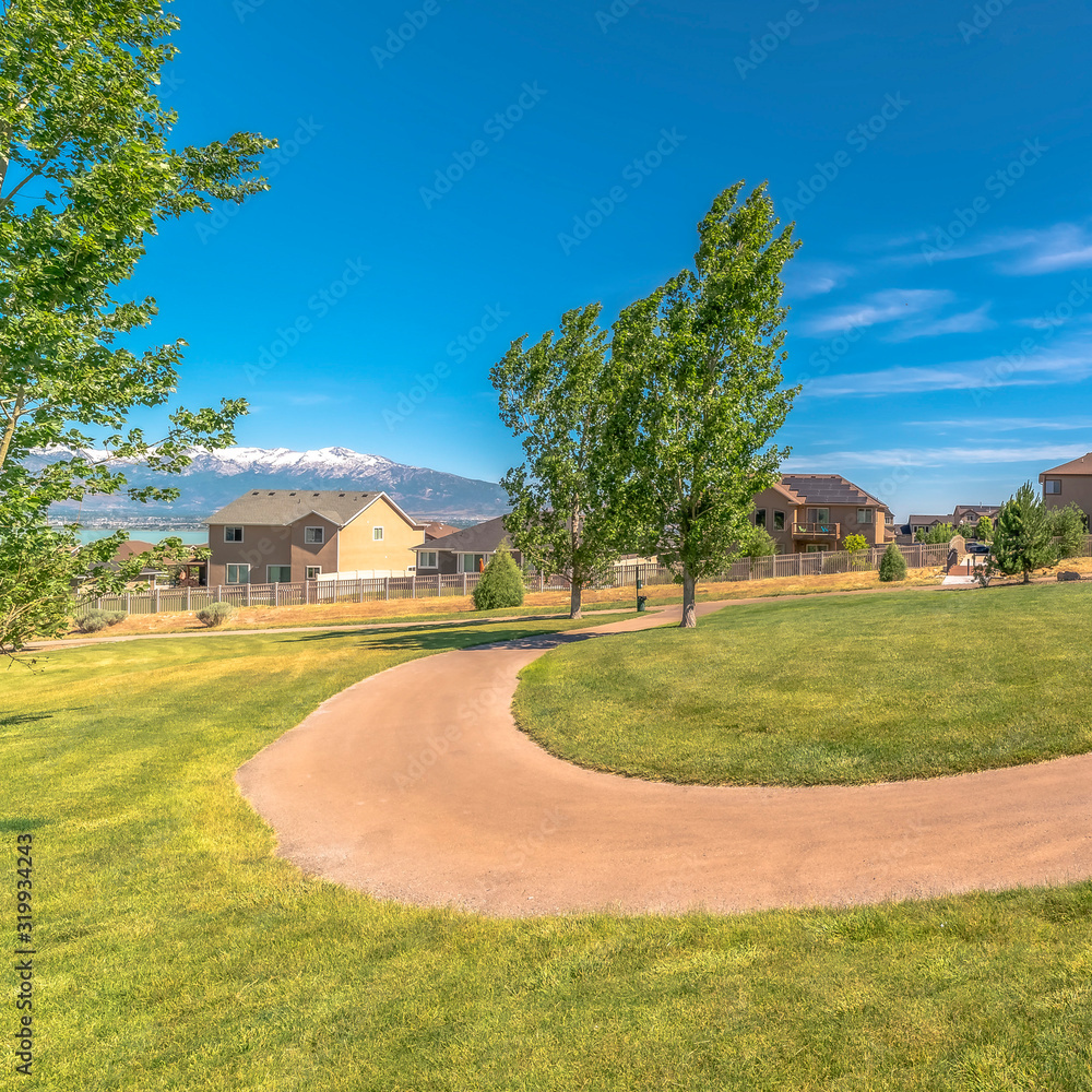 Square Pathway curving through vast grassy field with homes lake and mountain view