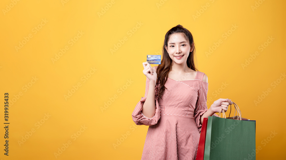 Beautiful asian woman are holding shopping bags with face happily in yellow seamless,isolated background. Shopping lifestyle, online shopping concept. Beautiful asian woman are holding shopping bags with face happily in yellow seamless,isolated background. Shopping lifestyle, online shopping concept.