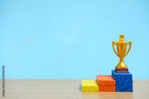 Golden trophy standing at colorful podium on wooden table