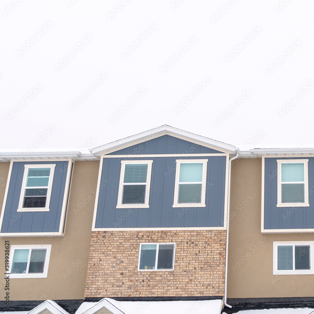 Photo Square Townhouses with snow covered gable roofs against cloudy sky at winter season