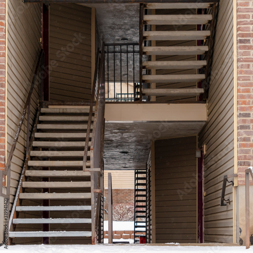 Square Residential building entrance with snow covered stairs and yard during winter