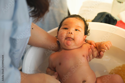 Baby is taking a shower. Mother is taking a shower to her baby in the house.