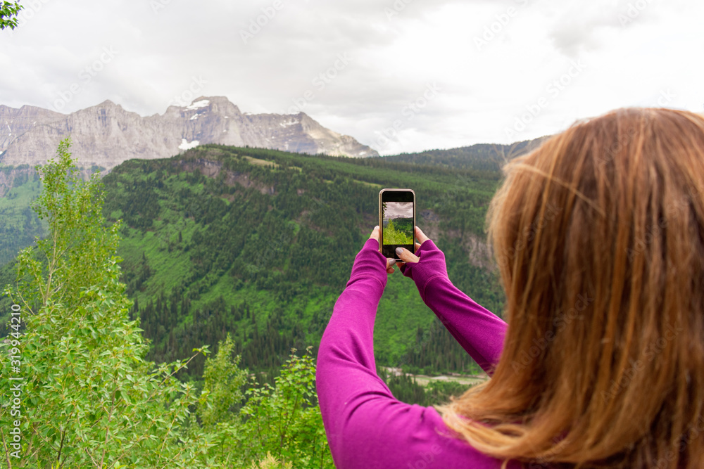 tourist taking photo of mountains with phone at Glacier National Park tourist taking photo of mountains with phone at Glacier National Park