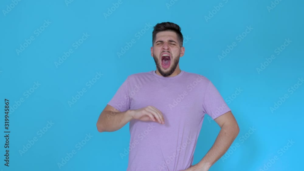 tired young man yawning and acting sleepy on blue background wearing t shirt tired young man yawning and acting sleepy on blue background wearing t shirt