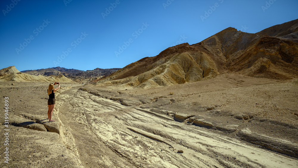 Attractive blonde woman standing in the landscape at Zabriskie Point, Death Valley National Park, California, USA