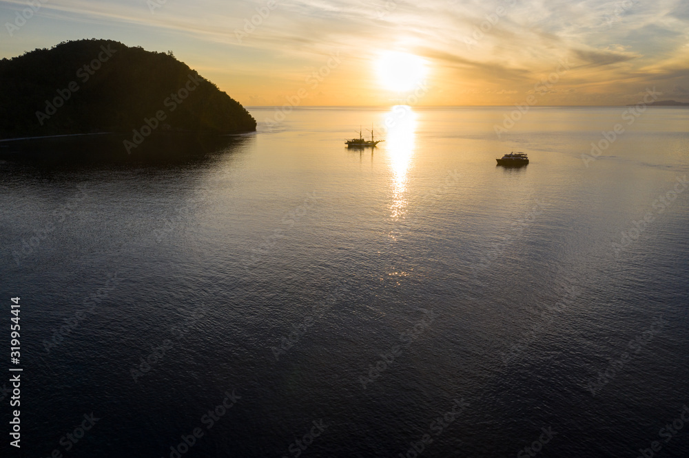 Sunrise silhouettes small ships as they rest in the glassy waters of Raja Ampat, Indonesia. This beautiful region is thought to be the world's epicenter of marine biodiversity.