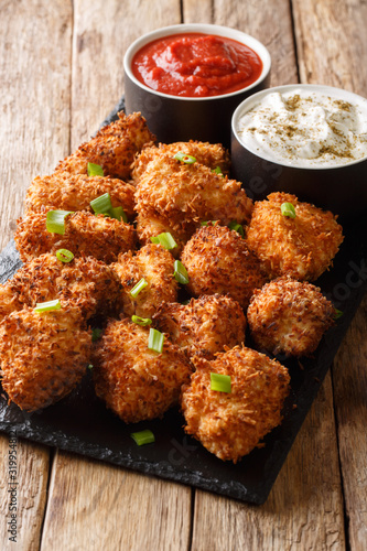 Crispy coconut chicken nuggets served with ketchup and mayonnaise close-up on a table. Vertical