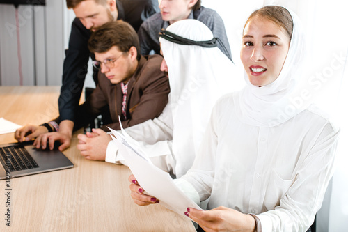 a young girl in a national headscarf holds a computer tablet at a meeting, in the background a meeting with an Arab representative. photo