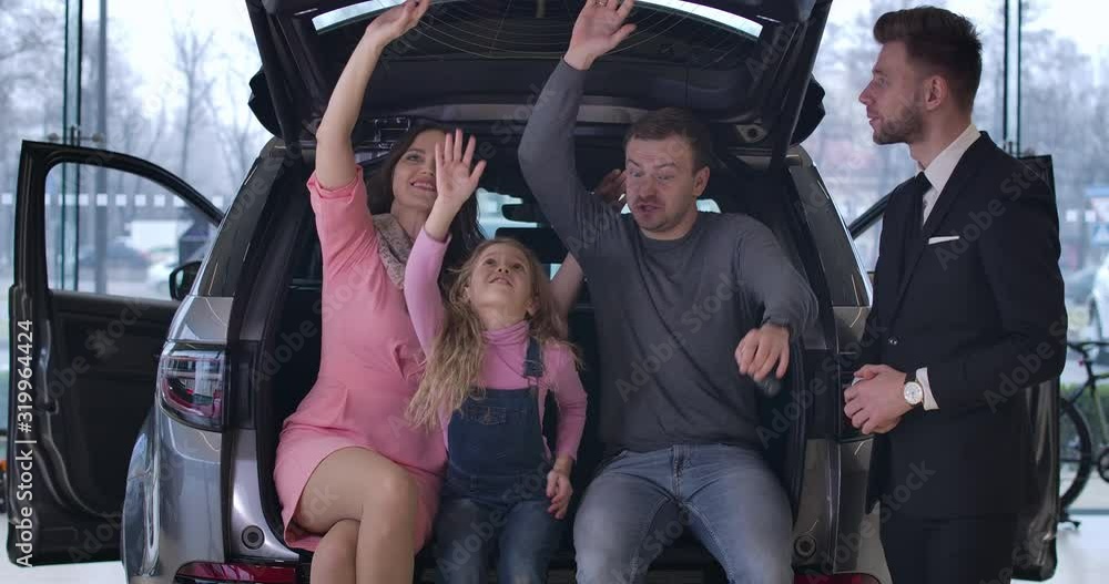 Four Caucasian people examining car salon. Young family sitting in car trunk, manager showing them interiors. Clients choosing new automobile in car dealership. Cinema 4k ProRes HQ. Four Caucasian people examining car salon. Young family sitting in car trunk, manager showing them interiors. Clients choosing new automobile in car dealership. Cinema 4k ProRes HQ.