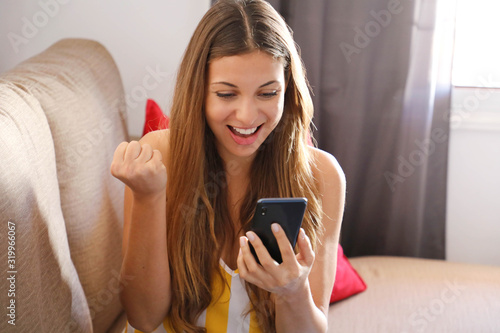 Bilde på lerret Happy overjoyed young woman holding mobile phone celebrating bid win game app vi