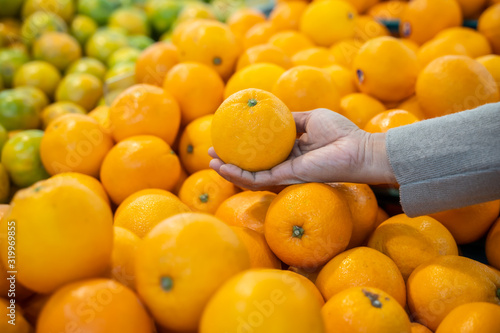 Woman hand choosing orange from the food counter at the supermarket. Shopping for fresh produce.