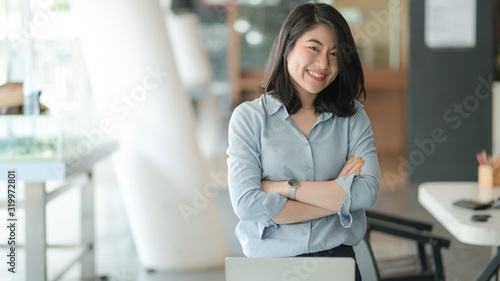Portrait of a young businesswoman standing with arms crossed and smiling in the office. Free Download Portrait of a young businesswoman standing with arms crossed and smiling in the office. - GFXLoad