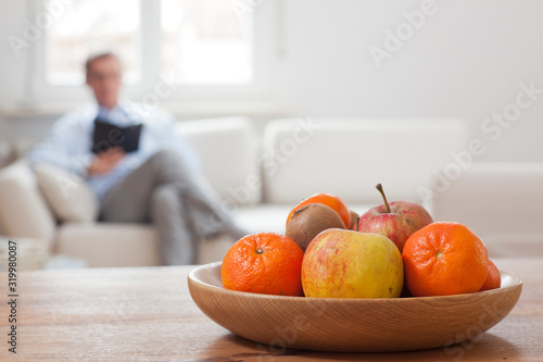 Fototapeta Naklejka Na Ścianę i Meble -  Man with tablet sitting in a living room with fruits in the foreground