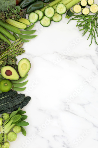 Plant based vegan health food with green vegetables & fruit forming a background border on marble. High in vitamins, antioxidants, minerals, fibre & healthy fats. Flat lay, top view, copy space.