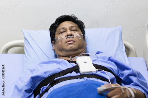 Asian Fat Man Sleeping On A Patient Bed With Breathing Equipment in Hospital.