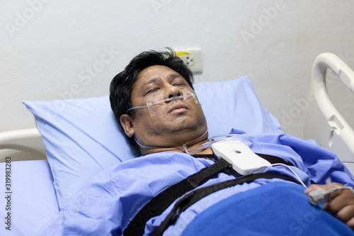 Asian Fat Man Sleeping On A Patient Bed With Breathing Equipment in Hospital.