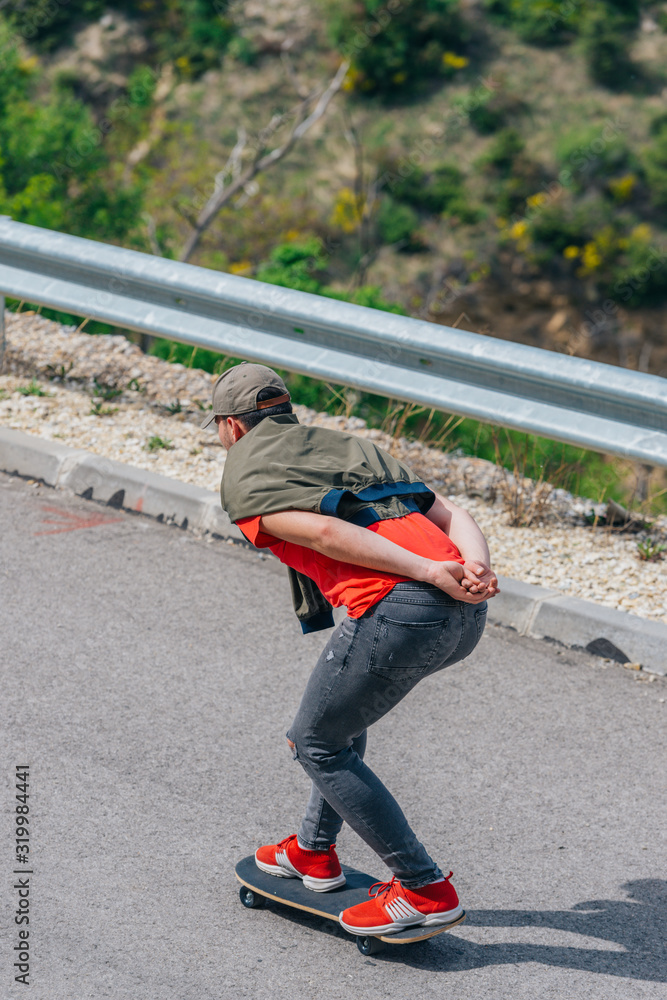 Tall fit male riding a longboard on an open road while performing a speed tuck.