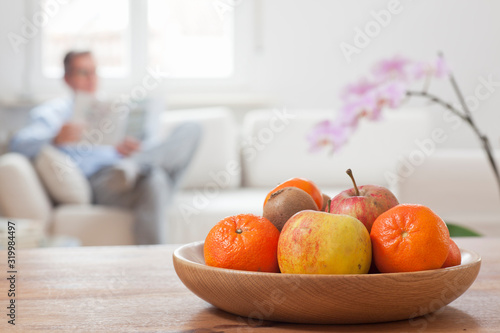 Fototapeta Naklejka Na Ścianę i Meble -  Mature man reading a newspaper on a couch with fruits in the foreground