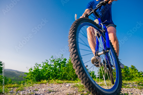 Close up photo from a mountain biker riding his bike ( bicycle) on rough rocky terrain on top of a mountain, wearing no safety equipment. Adrenalin junkie.