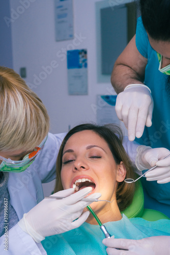 Professional male and female dentists examining woman's teeth in dental office