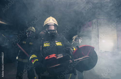 Portrait of fireman holding a rescue chainsaw in smoky garage of the fire department