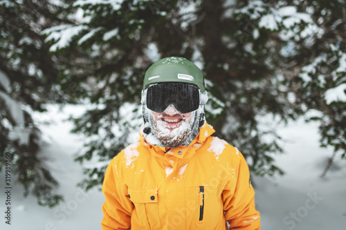 Cheerful smiling skier with snow on his bearded face after freeride on mountain forest. Closeup portrait.