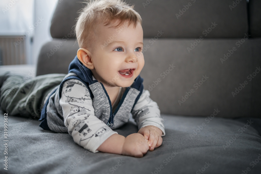 Cheerful happy little baby boy smiling and lying on stomach on couch in living room. Cheerful happy little baby boy smiling and lying on stomach on couch in living room.