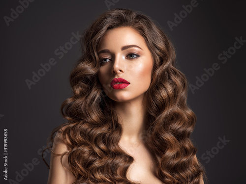 Beautiful woman with long brown hair. Beautiful face of an attractive model with red lipstick. Beauty of curly hair. Closeup portrait of caucasian stunning girl.