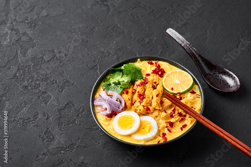 Ohn No Khao Swe in black bowl at dark slate background. Oh No Khao Suey is Coconut Milk Noodle Soup of myanmar cuisine with chicken meat and eggs. Burmese food. Copy space photo