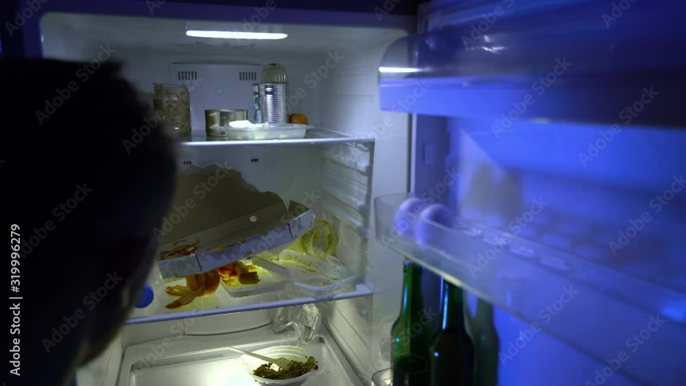Man looking for food in the fridge. The guy eats leftover food in the fridge and takes a bottle of beer. Night hunger. Hangover. Bachelor's fridge, view from behind. A dirty fridge. Man looking for food in the fridge. The guy eats leftover food in the fridge and takes a bottle of beer. Night hunger. Hangover. Bachelor's fridge, view from behind. A dirty fridge.