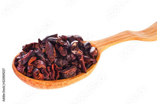 Cacao nibs in a wooden spoon isolated on a white background.