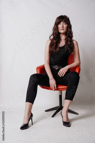 Young beautiful girl in business suit, shoes sitting on red chair, white background, business lady, young cute brunette