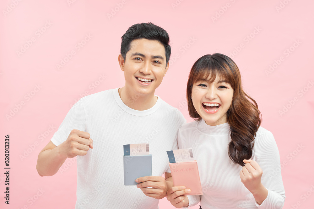 Portrait of successful lucky couple getting visa abroad holding raised fist showing passport with flying tickets shouting with wide open mouth isolated on pink background Portrait of successful lucky couple getting visa abroad holding raised fist showing passport with flying tickets shouting with wide open mouth isolated on pink background