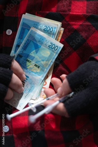 Fotografie Shekel money and syringes in the hands of a street trader.