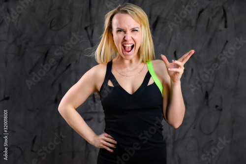 The concept of glamorous fitness. Photo of a beautiful pretty slim woman blonde sportswoman in a tracksuit on a gray background. Standing in different poses with emotions and a smile.