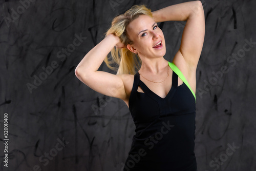 Photo of a beautiful pretty slim woman blonde sportswoman in a tracksuit on a gray background. The concept of glamorous fitness. Standing in different poses with emotions and a smile.