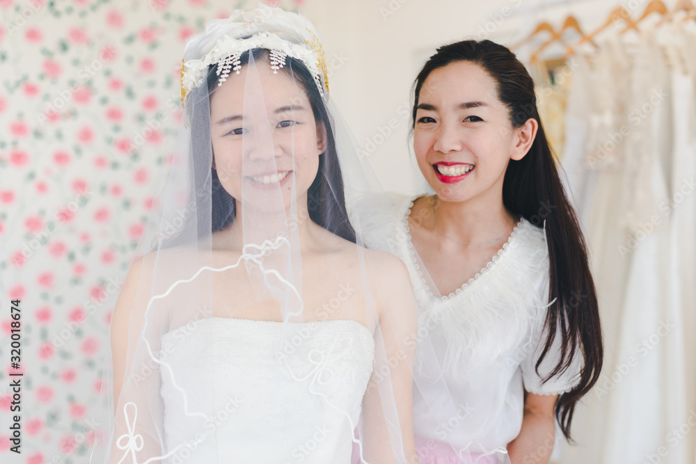 The bridesmaid is helping the beautiful bride wearing a white wedding dress in front of the mirror. The bridesmaid is helping the beautiful bride wearing a white wedding dress in front of the mirror.