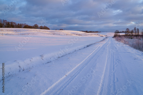 Winter morning, country road and fields covered with snow, in the distance you can see a hilly landscape. © Dainis