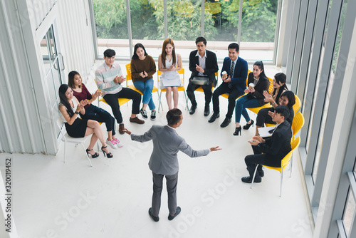 Asian Speaker male is speaking at seminars and workshops to the people in the meeting. By the participants of the seminar and training sitting round a semicircle. Top view.