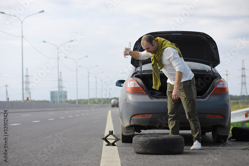 Replacing the wheel of a car on the road. A man doing tire work on the sidelines.