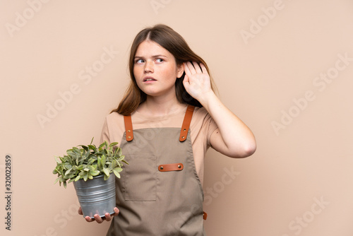 Ukrainian teenager gardener girl holding a plant listening something